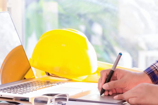 Maintenance worker with a notebook searching for CMMS software on a laptop in an office setting.