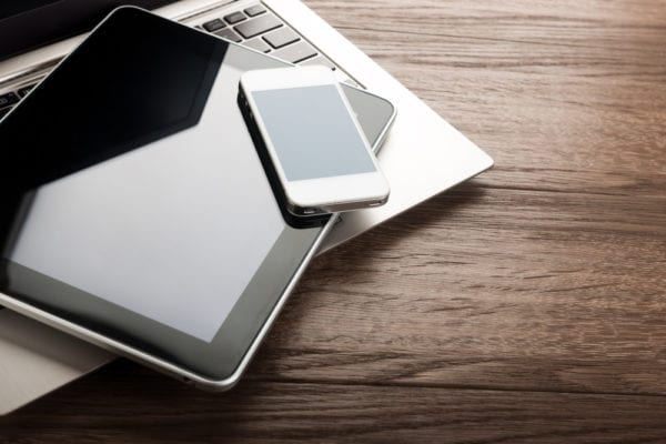 Laptop computer keyboard with tablet pc and smart phone on a wooden desk that could be used as part of a mobile maintenance software experience.