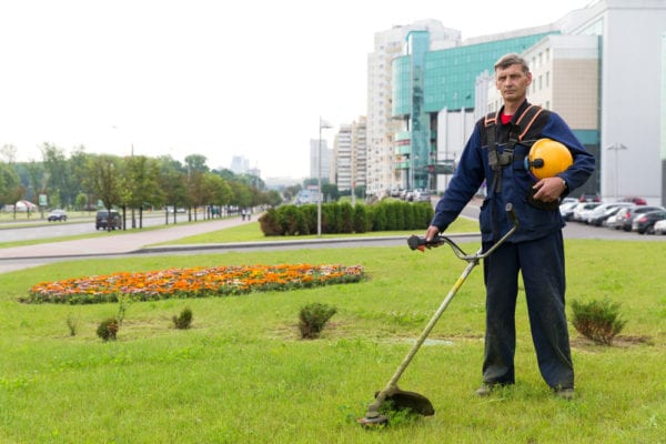 A middle-aged male facility maintenance tech with a gas trimmer standing on the lawn of a corporate property