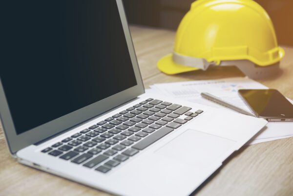 A laptop with a yellow hard hat in the background referencing the differences between CMMS and. EAM.