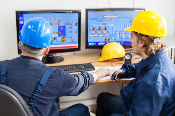 Rear view of maintenance workers in a control room looking at a computer monitor trying to understand the cause of unplanned production downtime