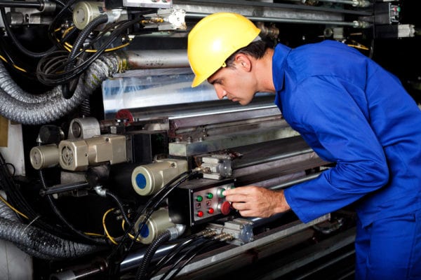 Young male technician inspecting a modern industrial printing machine as part of total productive maintenance