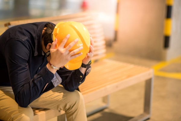 Maintenance worker feeling worried sitting on a bench with his head in his hands because he wasn't sure what to ask a CMMS vendor