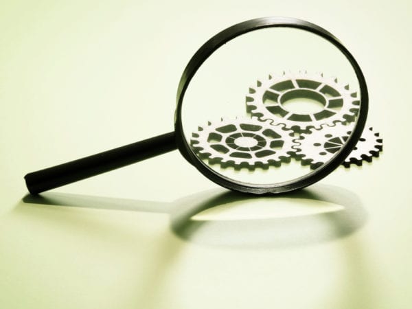 A magnifying glass enlarging an images of gears representing asset naming conventions as a part of asset identification