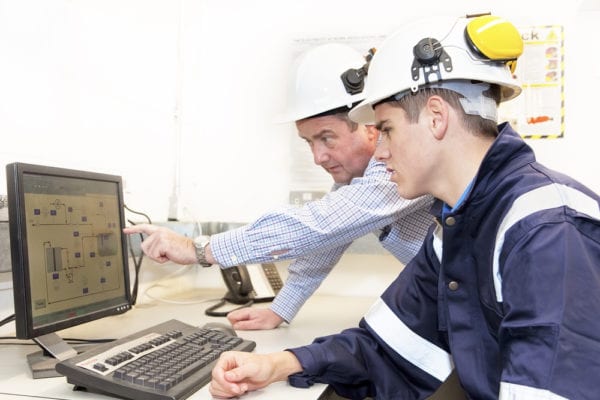Image_Failure Code Basics CMMS Failure Codes Older and younger men in hard hats discussing work together, older man pointing to area on a computer screen displaying failure codes.
