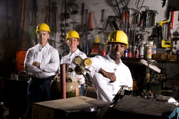 Three diversified employees in hard hats in a garage to represent maintenance department culture.