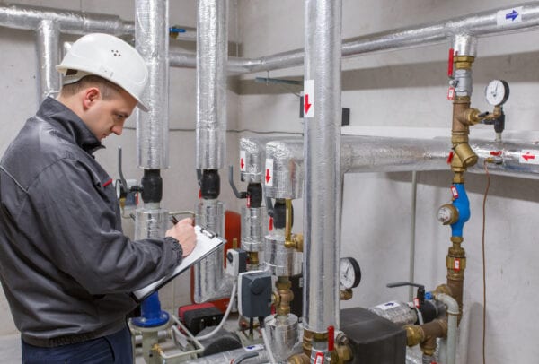 Young male technician recording meter readings from a heating system as part of a plan to improve preventive maintenance effectiveness.