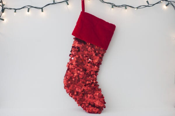 A red sequined stocking hanging under holiday lights on the wall to celebrate holidays while working remotely.