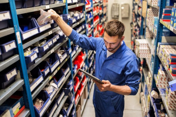 Young male stockroom worker auditing stock quantities as a first step in defining benchmarks for inventory management KPIs.