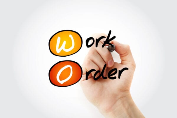 A hand writing Work Order to illustrate the about pros and cons of work order management systems.