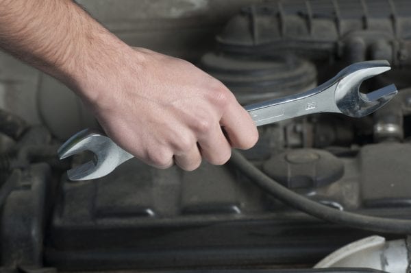 A male hand holding a crescent wrench tool in front of a motor.