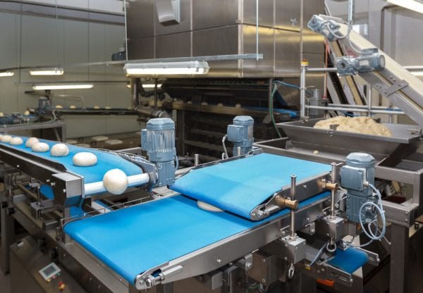 Bread dough being transported on a conveyor belt consistently due to proper food processing plant maintenance.