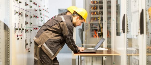 Two maintenance technicians in hard hats at a laptop in front of an asset adjusting power user CMMS settings.