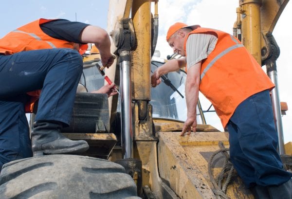 Two middle-aged maintenance technicians perform preventive maintenance on a construction vehicle as part of a preventive maintenance plan.