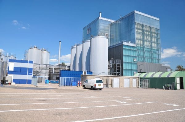 Large industrial building and parking lot with a white van on a sunny day, kept in working condition by a CMMS or CAFM.