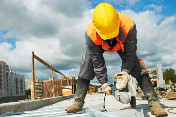 A construction worker in a hard hat using a concrete saw.