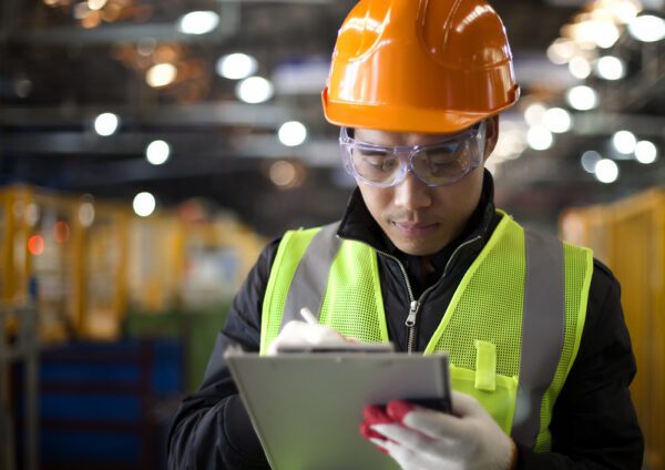 Maintenance worker with a clipboard checking off 5S tasks on a checklist in a warehouse.