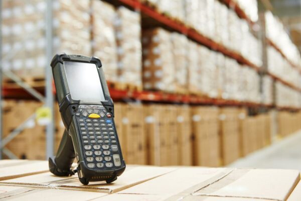 A mobile computer with integrated barcode scanner displayed on top of boxes in a warehouse.