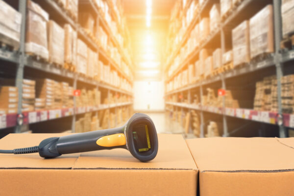 A wired barcode scanner laying on cardboard boxes in a warehouse.