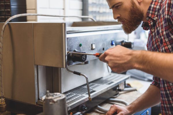 Man fixing an espresso machine in response to a customer's service request for maintenance.