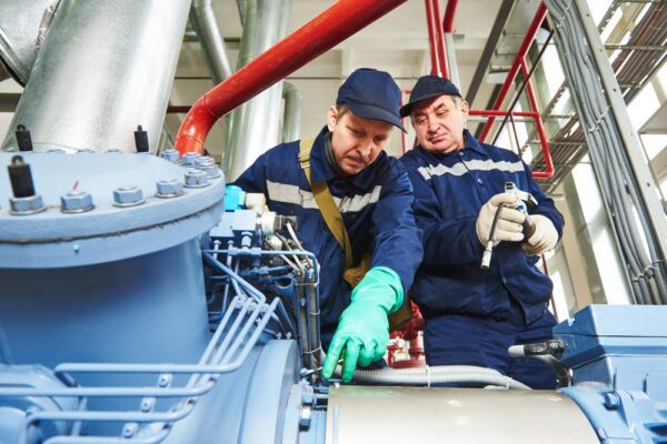 Two technicians discussing and working on a machine as they follow preventive maintenance best practices, part of CMMS best practices for use.