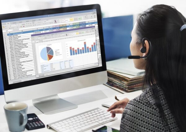 Woman with headset looking at desktop screen with charts and data from both CMMS and ERP software.