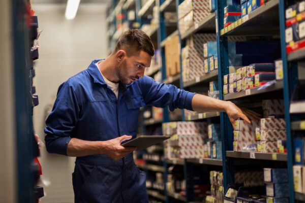 Maintenance worker checking MRO inventory on shelf and using tablet to look up vendor contact info.