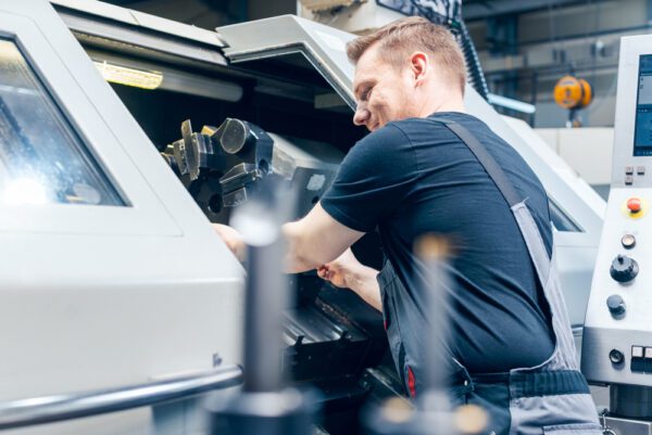 Young male machine operator removing product from a CNC machine with high availability