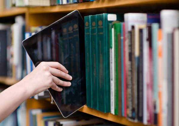 Hand pulling a tablet computer off a library shelf filled with books
