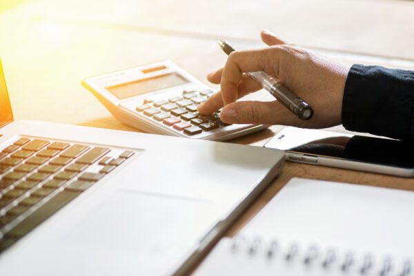 Person's hand calculating CMMS pricing on a calculator at a desk with laptop