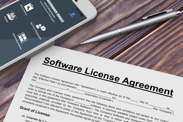 A CMMS software license agreement contract on a table with the FTMaintenance Select app on a phone.