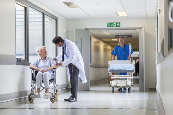 Doctor speaking with older woman patient in a wheelchair in a hospital wing.