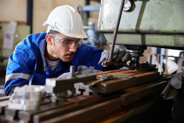 Technician inspecting a lathe in a machine shop to determine whether to repair or replace it.