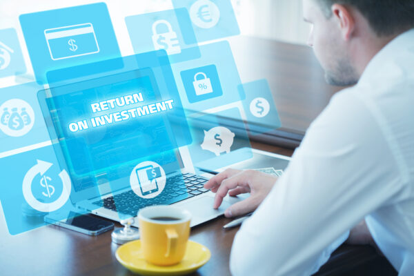Return on investment concept shown by white collar man sitting at a laptop with an overlay of cost-related graphics
