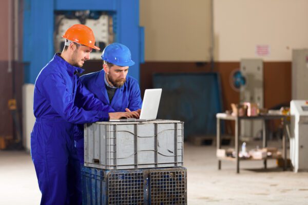 Medium shot of a maintenance technician assisting another technician in using a CMMS to increase user adoption.