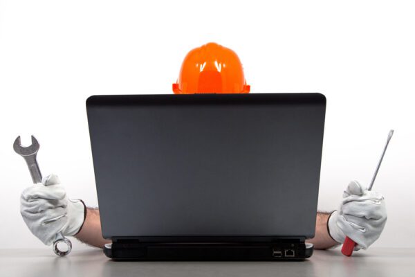 A maintenance technician holding tools sitting behind a laptop.