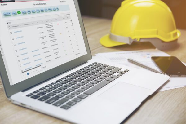 Close up of CMMS software on a laptop sitting on a desk with a hard hat.