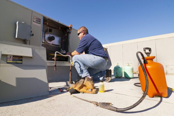 Male HVAC specialist on a roof repairing a cooling system.