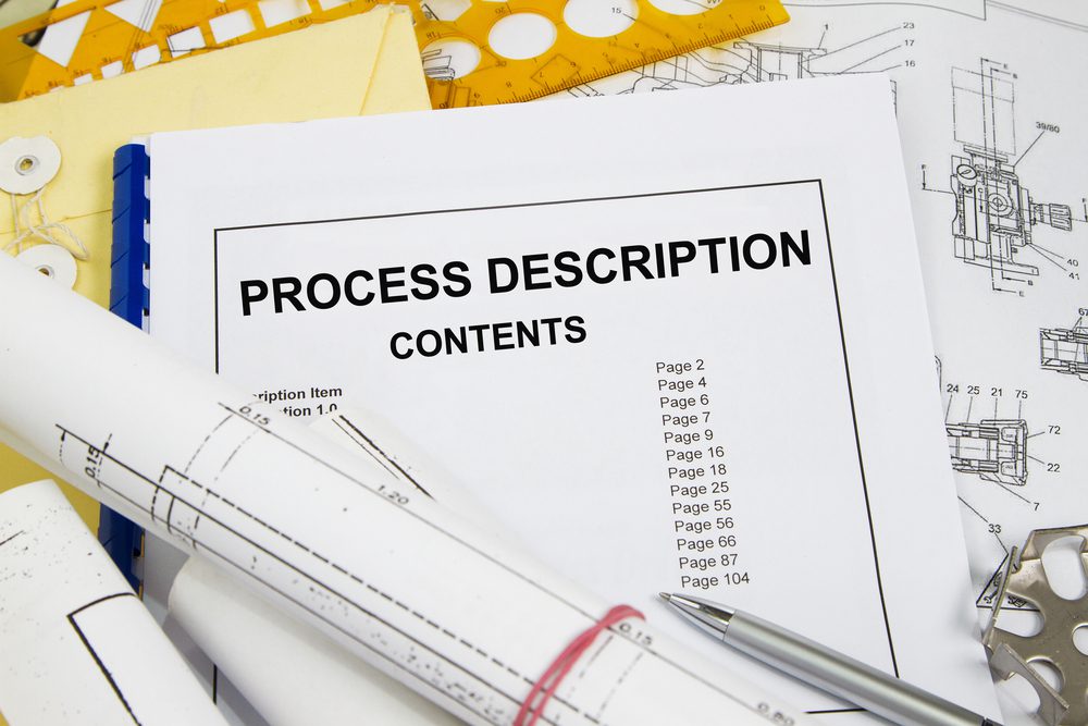 A bound process description manual laying on a cluttered desk with other maintenance and operations documents