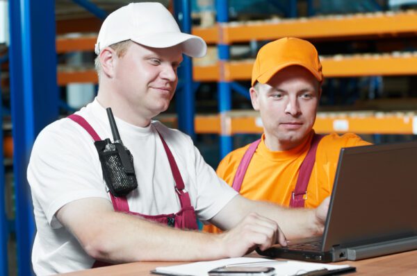 Two technicians standing at a laptop in a warehouse.