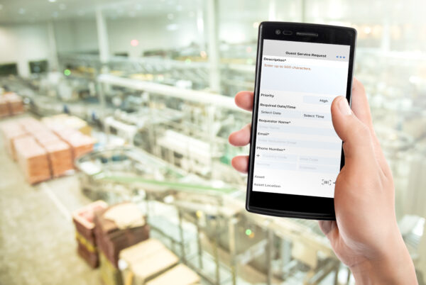 Hand holding a smartphone with the FTMaintenance Select mobile app open to a request submission form in a packaging facility.