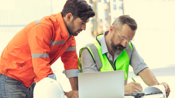 Senior male operations engineer reviews asset management report with junior engineering manager.