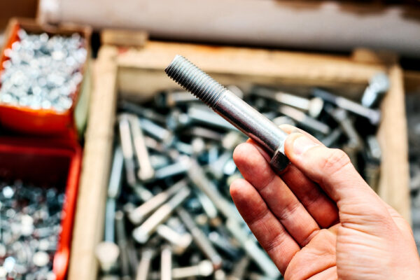 Close-up shot of a hand holding a bolt in front of a large bin of similar inventory items.