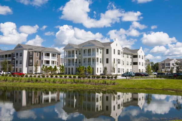 Apartment buildings with reflection in nearby pond and blue sky keep functional through property maintenance