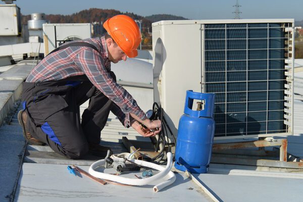 Young male HVAC technician performing time-based maintenance hose replacement on a rooftop air handler.
