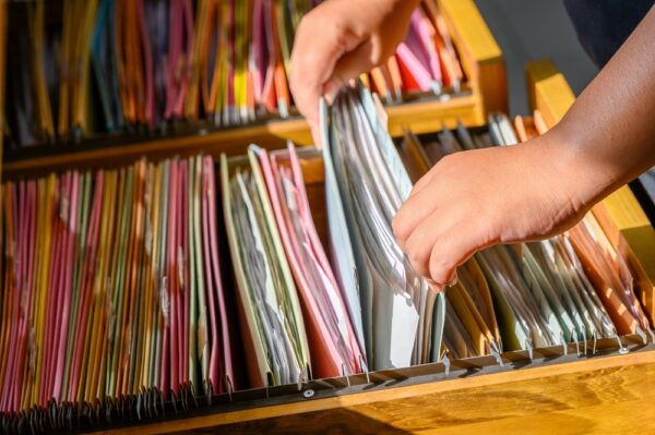 Close-up shot of person placing paper work orders in a filing cabinet drawer.